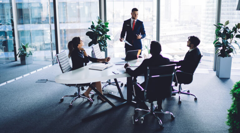 Four colleagues in a meeting at an oval table in a high rise conference room with glass walls