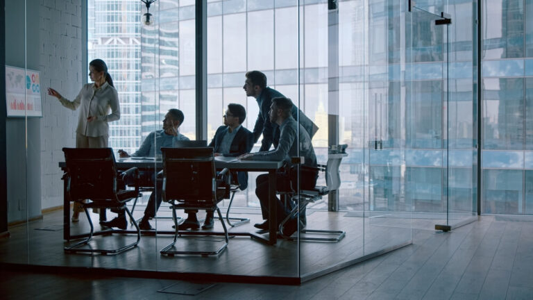 Five coworkers discussing infographics in a glass conference room